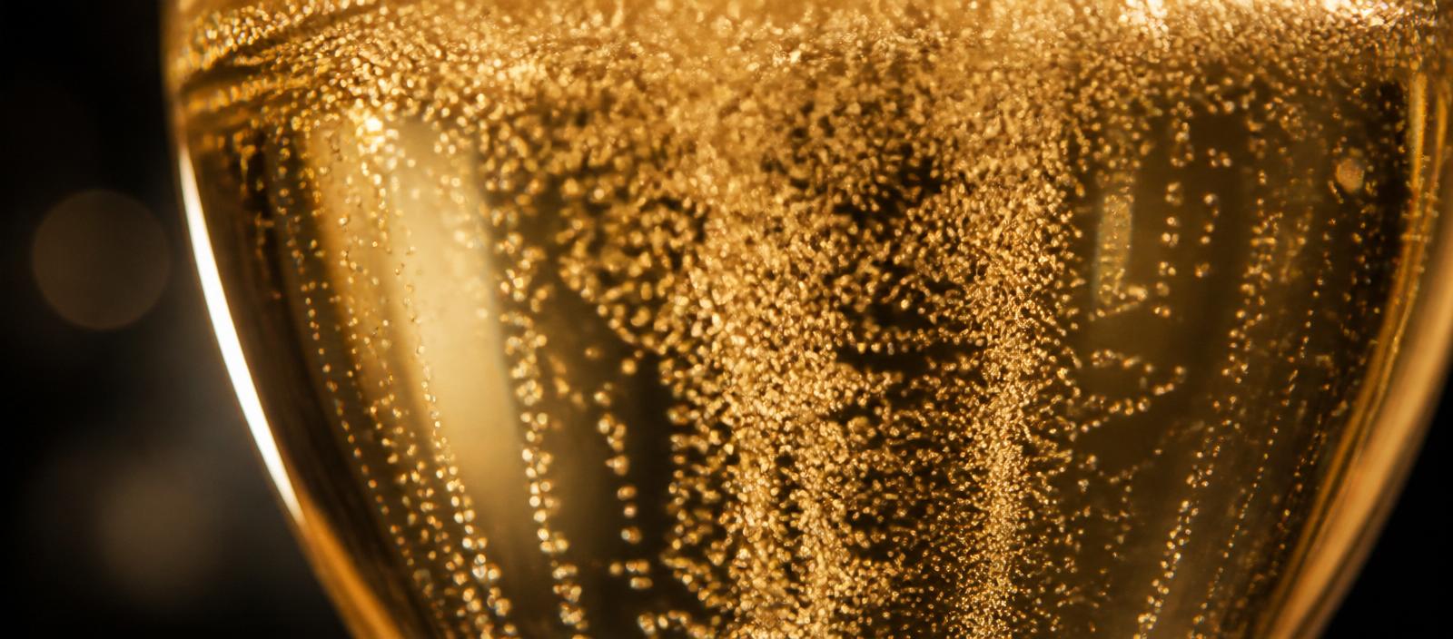 Närbild på fina, gyllene bubblor i ett glas mousserande vin